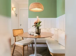 Sala de jantar moderna com mesa redonda de madeira, parede verde suave e luminária de palha, exemplo de decoração funcional e acolhedora.