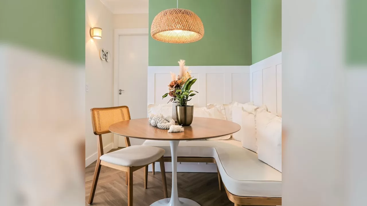 Sala de jantar moderna com mesa redonda de madeira, parede verde suave e luminária de palha, exemplo de decoração funcional e acolhedora.